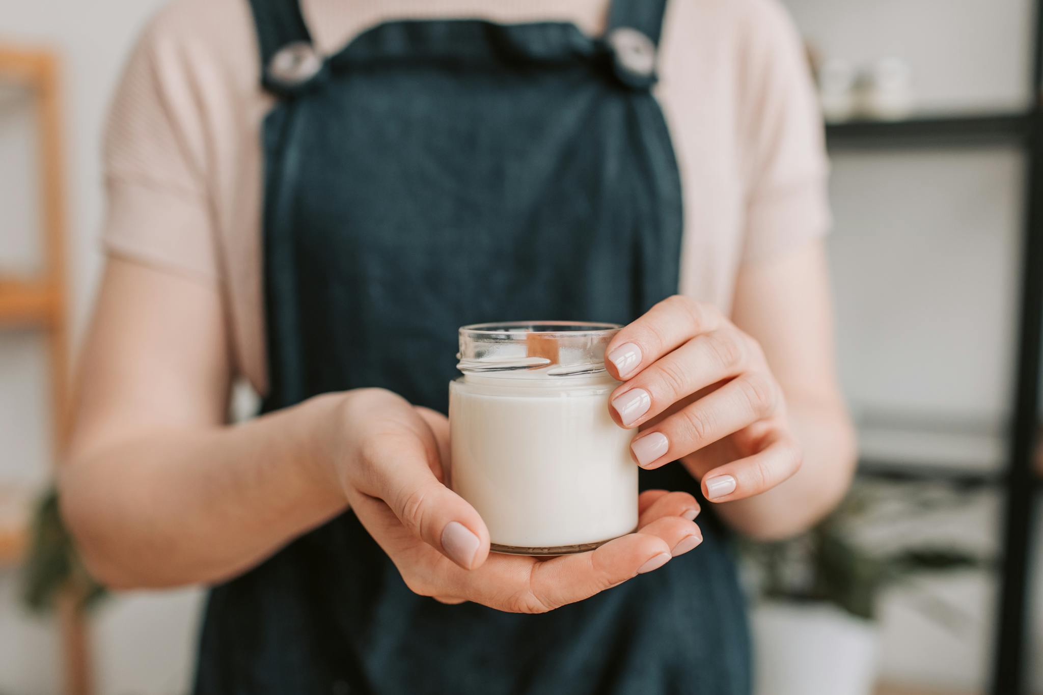 A person holding a glass jar containing a wax candle, showcasing natural light and DIY aesthetic.
