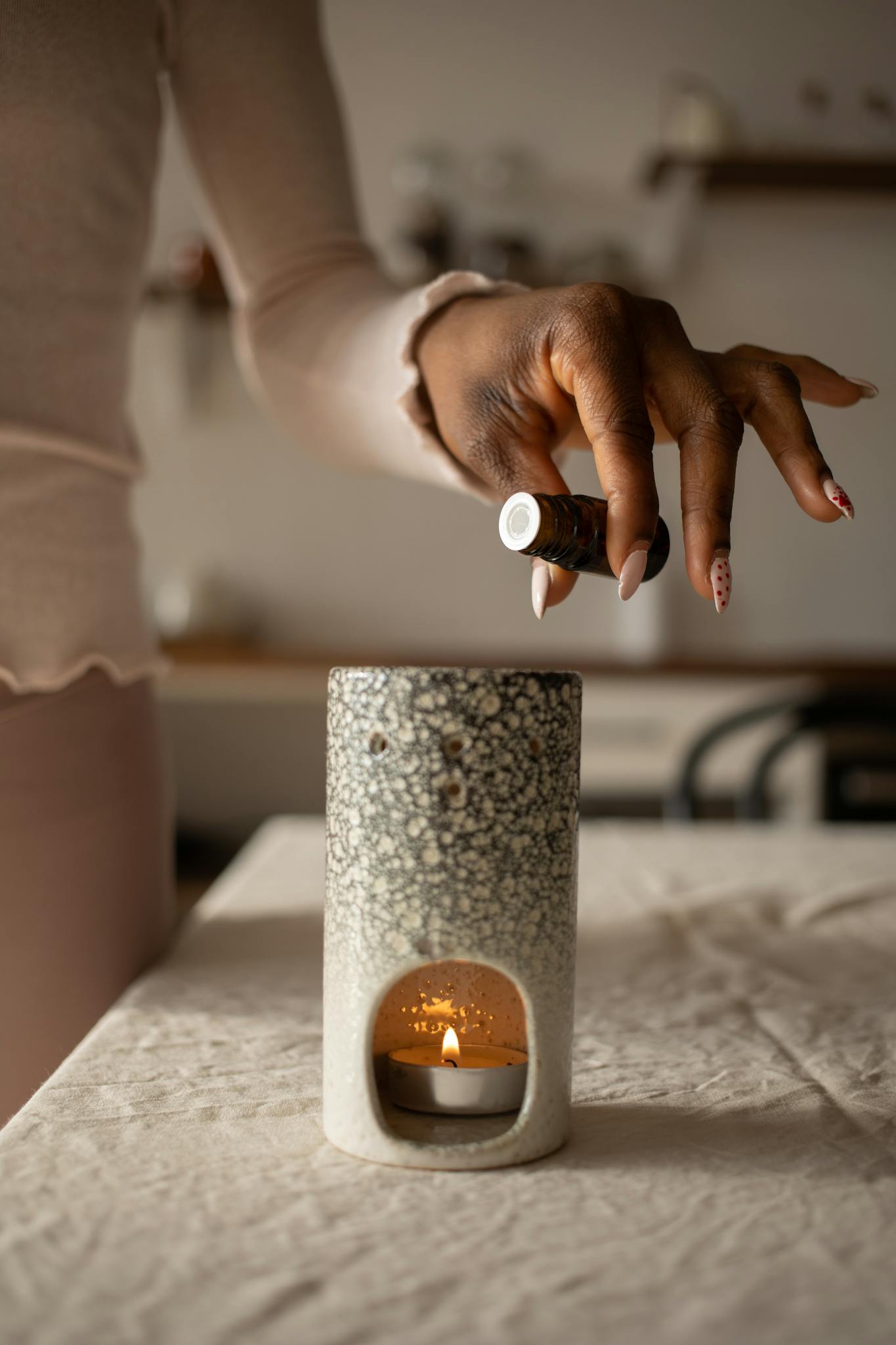 A woman pours essential oil into a ceramic candle burner creating a calming ambiance.