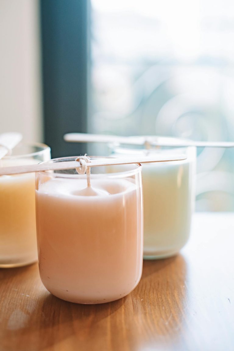 Close-up of pastel-colored handmade candles with wooden wicks, beautifully crafted on a wooden table.