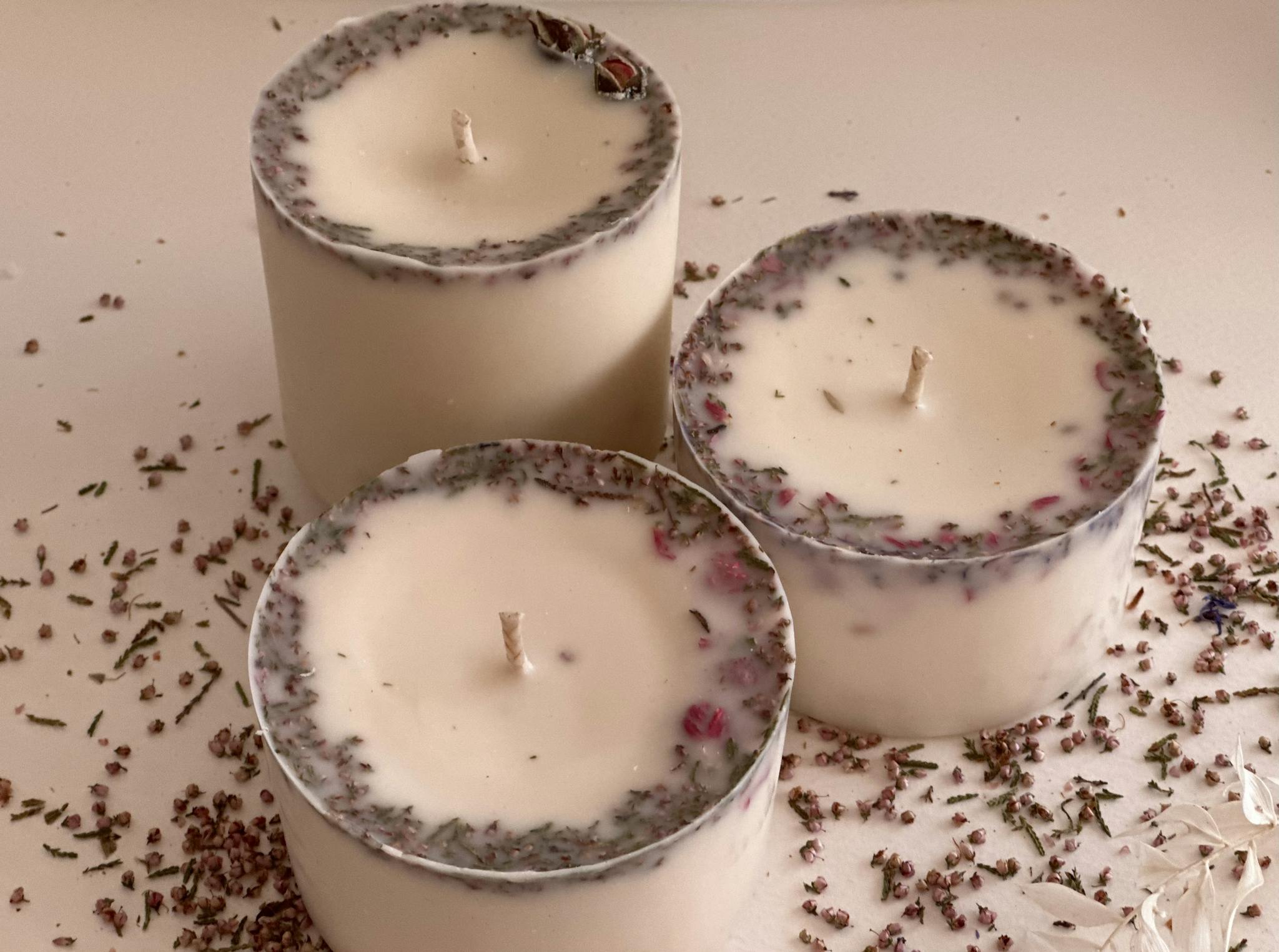 Close-up of three scented candles decorated with botanical herbs for aromatherapy.