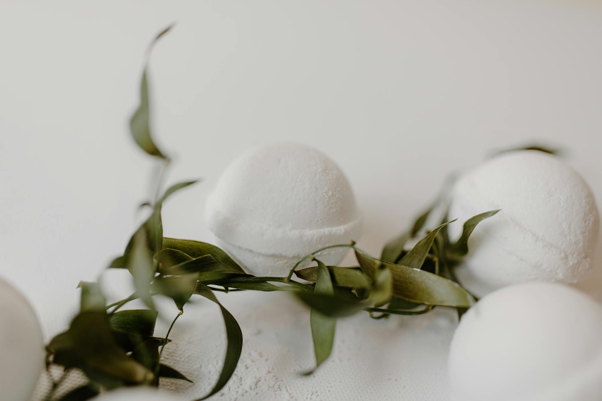 Minimalist bath bombs with eucalyptus leaves on a clean white surface for a serene bath experience.